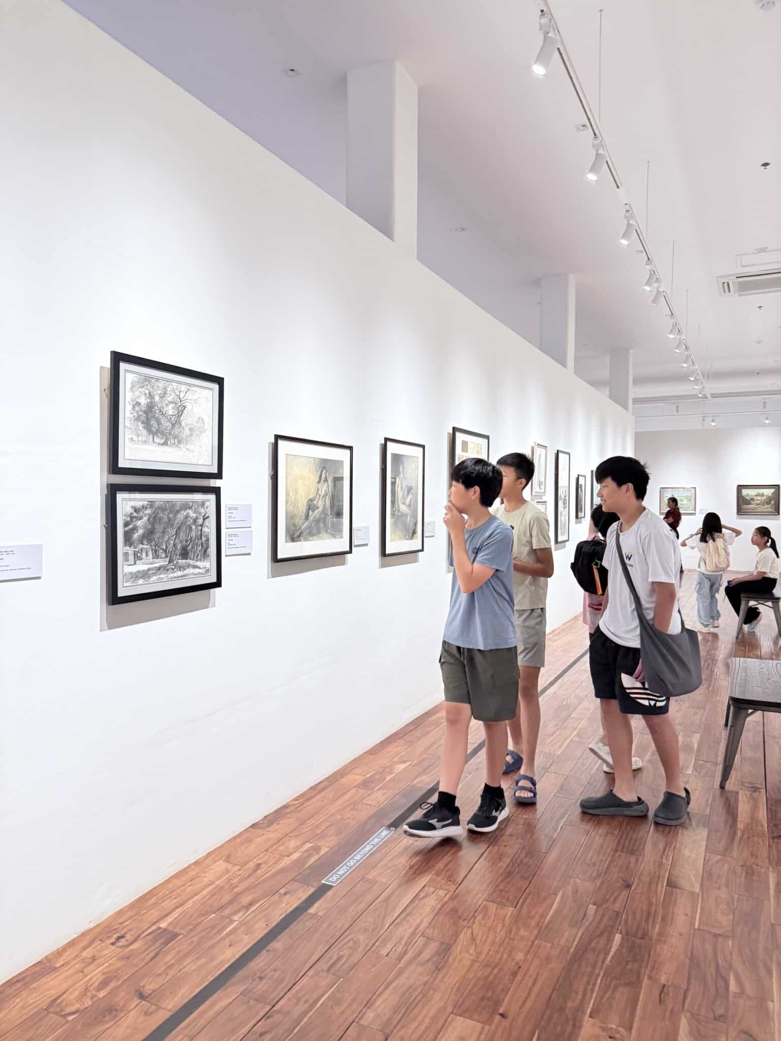 三位孩子專心看展間牆上的畫作，認真閱讀英文作品說明